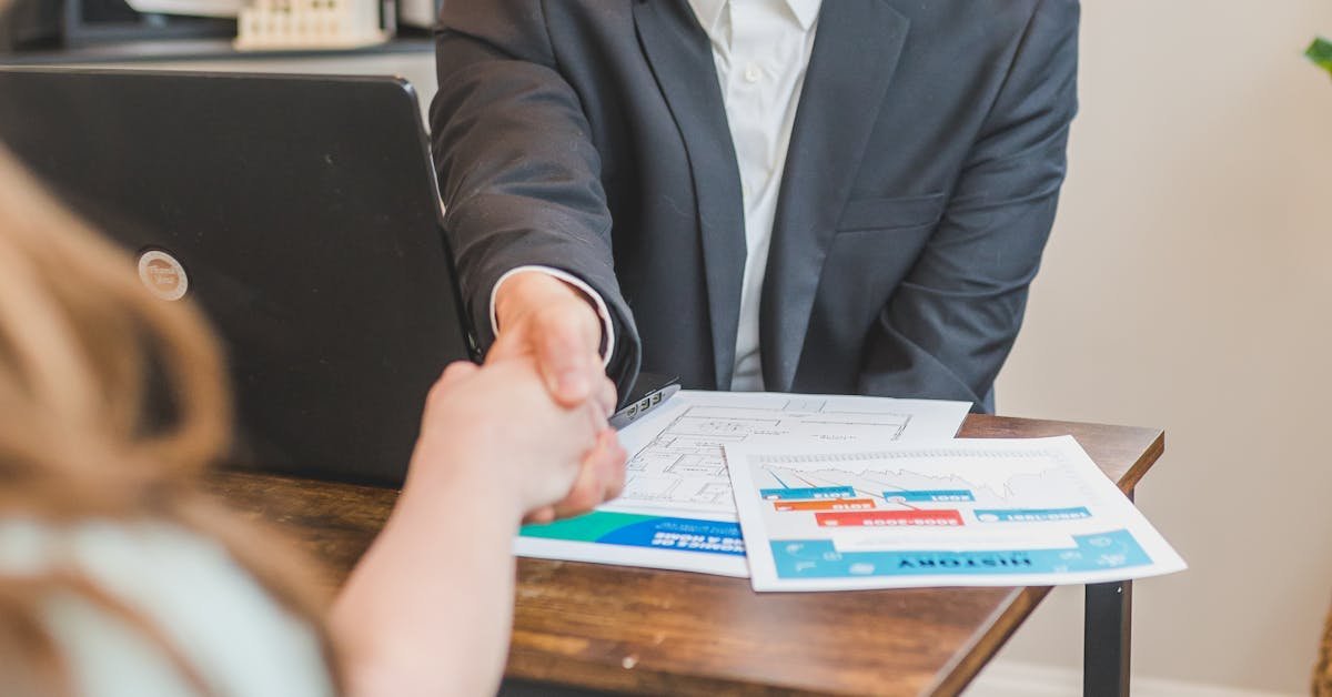 Professional surveyor in a suit shaking hands with a client across a desk, representing the instruction and timeline process of a commercial building survey